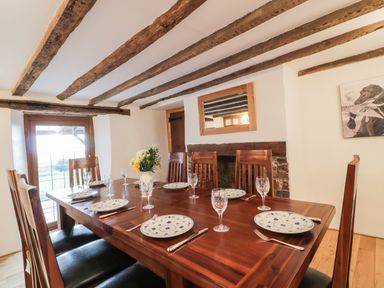 A dining room with a wooden table set with plates and glasses and wooden beams on the ceiling at Lower West Curry Farmhouse in Launceston