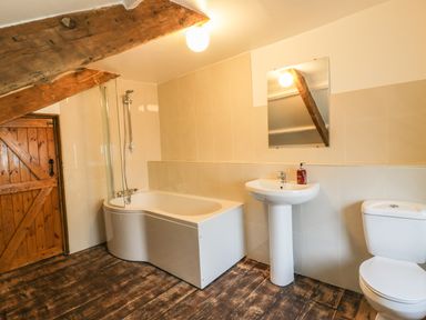 A bathroom with a bathtub shower combo sink toilet wooden door and exposed wooden beams at Lower West Curry Farmhouse in Launceston