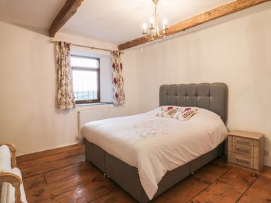 A bedroom with a double bed wooden floor side table window with curtains and ceiling beams at Lower West Curry Farmhouse Launceston