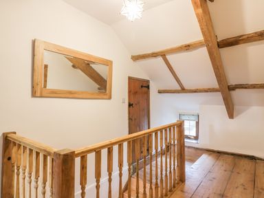A hallway with wooden railing mirror wooden door and exposed ceiling beams at Lower West Curry Farmhouse Launceston