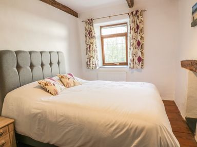 A bedroom with a bed two floral pillows wooden floor and a window with floral curtains at Lower West Curry Farmhouse in Launceston