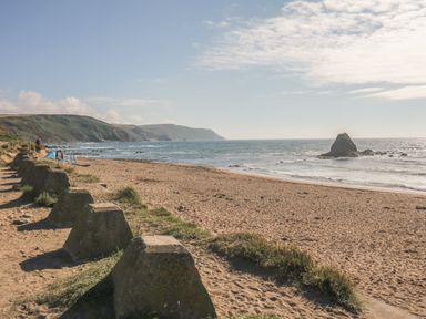 A sandy beach with sea and rocky coastline in the distance at Lower West Curry Farmhouse in Launceston