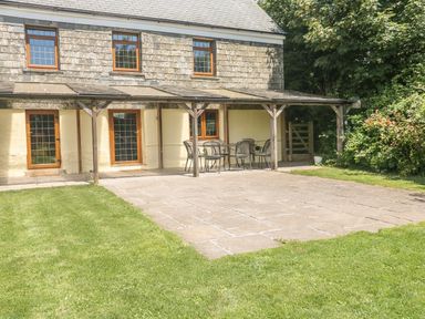 An outdoor patio area with stone tiles and metal chairs and table next to a house with wooden framed windows and doors at Lower West Curry Farmhouse in Launceston