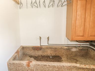 A stone utility sink with two taps and metal hangers above in a room with wooden cabinet at Lower West Curry Farmhouse in Launceston