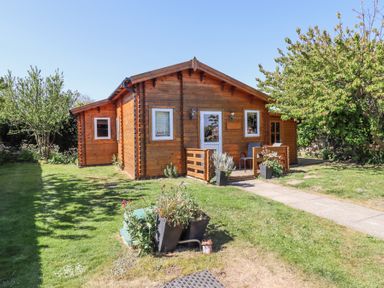 A wooden cabin with white framed windows and a small porch in a grassy garden with trees at Aurora Skies in Cresswell near Morpeth