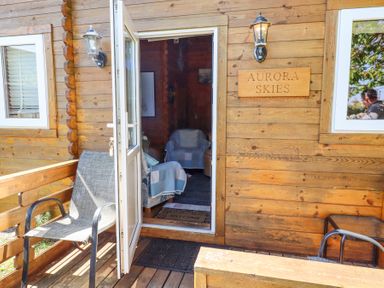 A wooden cabin entrance with an open door two chairs and a sign reading Aurora Skies at Aurora Skies in Cresswell near Morpeth