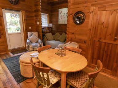 A wooden dining table with four chairs in a living room with a sofa armchair and door at Aurora Skies in Cresswell near Morpeth