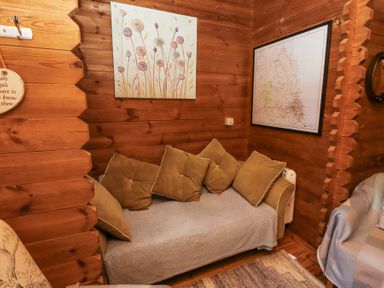 A wooden room with a sofa covered by a throw and cushions a floral painting and a framed map on the walls at Aurora Skies in Cresswell near Morpeth