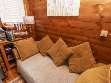 A small corner seating area with brown cushions next to a wooden shelf with books and a lamp at Aurora Skies in Cresswell near Morpeth