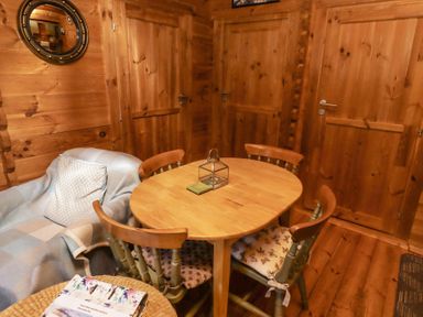 A wooden dining table with four chairs and a small lantern in a wooden room with a plaid covered armchair and round mirror on the wall at Aurora Skies in Cresswell near Morpeth