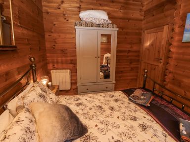 A bedroom with a bed covered with floral bedding a wardrobe with a mirror and wooden walls at Aurora Skies in Cresswell near Morpeth