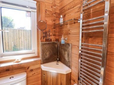 A small corner sink with soap and hand gel a towel radiator and a window in a wooden bathroom at Aurora Skies in Cresswell near Morpeth