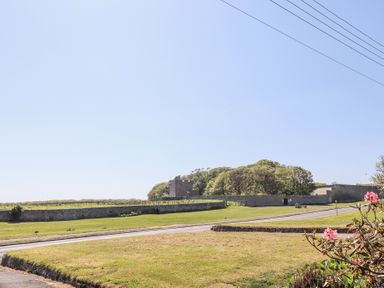 A grassy open area with a road and stone walls with trees and a stone building in the background at Aurora Skies in Cresswell near Morpeth