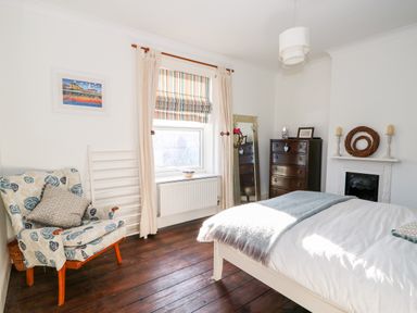 A bedroom with a bed chair chest of drawers and a window at Carrstone Cottage in Heacham