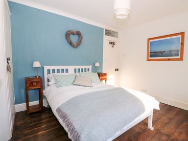 A bedroom with a double bed two bedside tables and lamps a heart-shaped decoration on a blue wall and a framed picture at Carrstone Cottage in Heacham