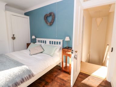 A bedroom with a bed pillows lamps wooden side tables and a heart-shaped wall decoration at Carrstone Cottage in Heacham