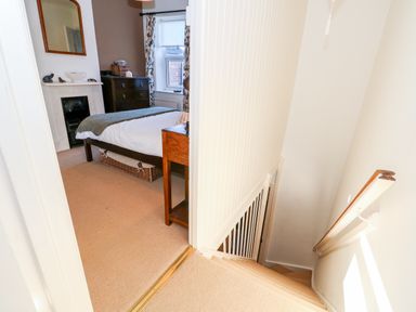 A bedroom with a bed dresser and a fireplace next to a staircase at Carrstone Cottage in Heacham