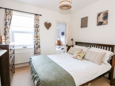 A bedroom with a bed with striped pillows and green throw blanket next to a window with floral curtains at Carrstone Cottage in Heacham