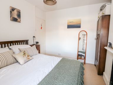 A bedroom with a bed pillows blanket a bedside table a mirror a wardrobe and two paintings at Carrstone Cottage in Heacham