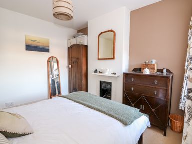 A bedroom with a bed a wooden wardrobe a tall mirror a mantelpiece with a mirror above and a wooden chest of drawers at Carrstone Cottage in Heacham