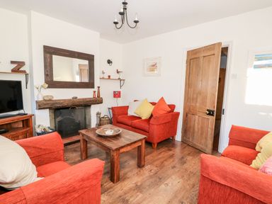 A living room with red sofas wooden coffee table and a fireplace at Carrstone Cottage in Heacham