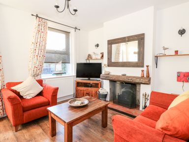A living room with two red armchairs a wooden coffee table a fireplace and a TV at Carrstone Cottage in Heacham