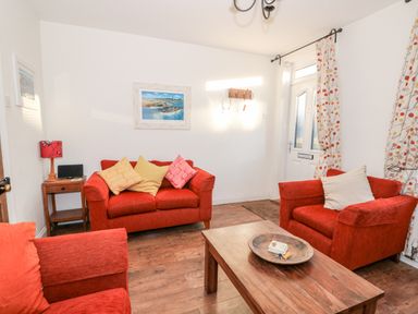 A living room with red sofas wooden coffee table side table with lamp and framed pictures on the walls at Carrstone Cottage Heacham