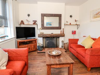 A living room with two red sofas a wooden coffee table a fireplace a television and shelves with decorative items at Carrstone Cottage in Heacham