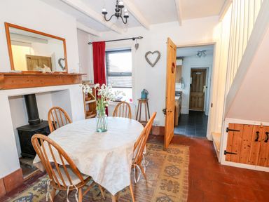 A dining room with a table and chairs a wood stove under a wooden mantel and a doorway leading to a kitchen at Carrstone Cottage in Heacham