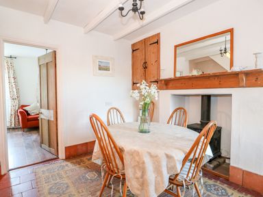 A dining room with a round table and four chairs a vase with flowers on the table a fireplace with a wood stove and a mirror above at Carrstone Cottage in Heacham