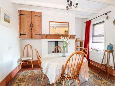 A dining room with a round table covered with a tablecloth and wooden chairs at Carrstone Cottage in Heacham