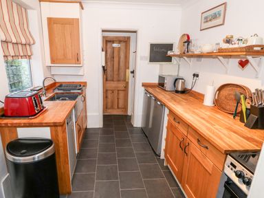 A kitchen with wooden countertops and cabinets a red toaster a sink a microwave kettle and knives at Carrstone Cottage in Heacham