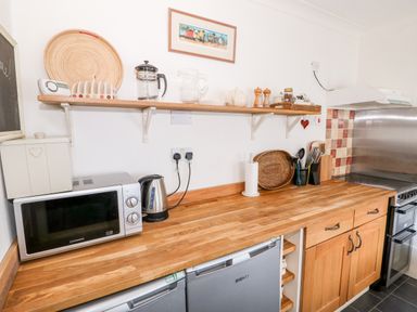 A kitchen countertop with a microwave kettle paper towel holder and utensils at Carrstone Cottage in Heacham