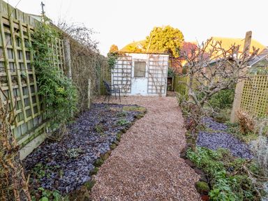 A garden with gravel pathway trees and a shed at Carrstone Cottage in Heacham