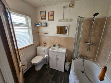 A bathroom with a toilet sink and bathtub with shower at Carrstone Cottage in Heacham
