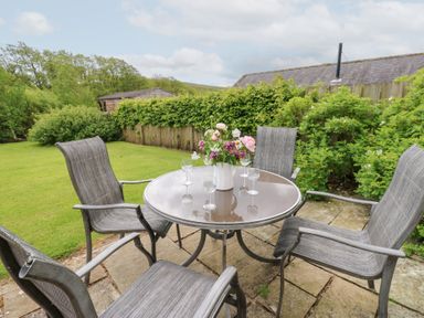 A table with chairs and a vase of flowers in the garden at Shepherds Burn Cottage in Bellingham