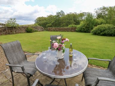A table with chairs and flowers in a garden at Shepherds Burn Cottage Bellingham