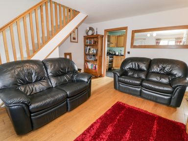 A living room with two black leather sofas a wooden bookshelf and a red rug at 6 Stad Yr Ysgol in Manod near Blaenau Ffestiniog