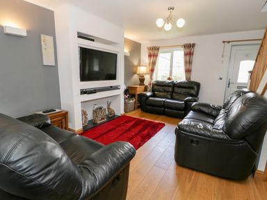 A living room with black leather sofas a red rug a wall-mounted TV and wooden flooring at 6 Stad Yr Ysgol in Manod near Blaenau Ffestiniog