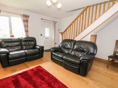 A living room with two black leather sofas a wooden staircase and a red rug at 6 Stad Yr Ysgol in Manod near Blaenau Ffestiniog