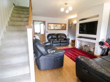 A living room with black leather sofas a red rug a wall-mounted television and stairs at 6 Stad Yr Ysgol in Manod near Blaenau Ffestiniog