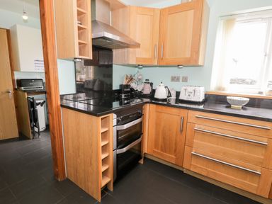 A kitchen with wooden cabinets a black countertop an oven a stove a kettle a toaster and a bowl on the counter at 6 Stad Yr Ysgol in Manod near Blaenau Ffestiniog