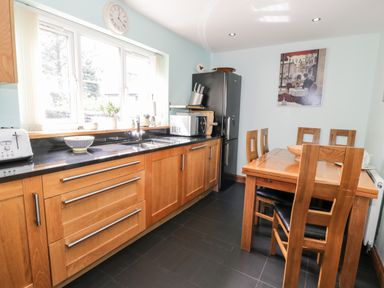 A kitchen with wooden cabinets a black countertop a dining table with wooden chairs and a black refrigerator at 6 Stad Yr Ysgol in Manod near Blaenau Ffestiniog