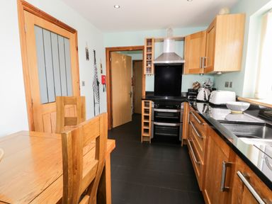A kitchen with wooden cabinets black countertops a dining table wooden chairs and appliances at 6 Stad Yr Ysgol Manod near Blaenau Ffestiniog