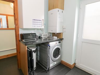 A utility room with a washing machine a bread box a microwave and a door at 6 Stad Yr Ysgol in Manod near Blaenau Ffestiniog