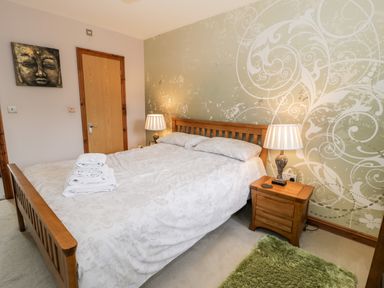 A bedroom with a wooden bed and bedside table with a lamp at 6 Stad Yr Ysgol in Manod near Blaenau Ffestiniog