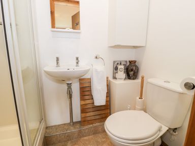 A small bathroom with a white sink a towel on a wooden rack a toilet and a shower with glass doors at 6 Stad Yr Ysgol Manod near Blaenau Ffestiniog
