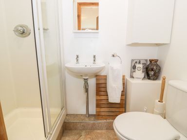 A bathroom with a shower, sink, toilet, towel hanging on a wooden rack, and decorative items on a shelf at 6 Stad Yr Ysgol in Manod near Blaenau Ffestiniog