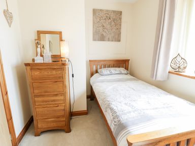 A bedroom with a wooden bed and chest of drawers with a mirror and lamp at 6 Stad Yr Ysgol in Manod near Blaenau Ffestiniog