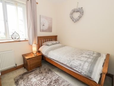 A bedroom with a single wooden bed a nightstand with a lamp a window and a heart decoration on the wall at 6 Stad Yr Ysgol Manod near Blaenau Ffestiniog